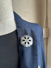 Close-up of a decorative brooch on a navy blue garment with a neutral background