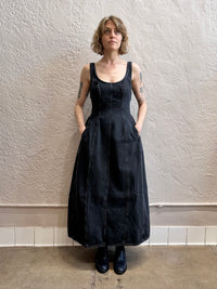 Person wearing a black denim dress standing against a textured wall.