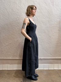 Woman wearing a black denim dress standing against a textured white wall.