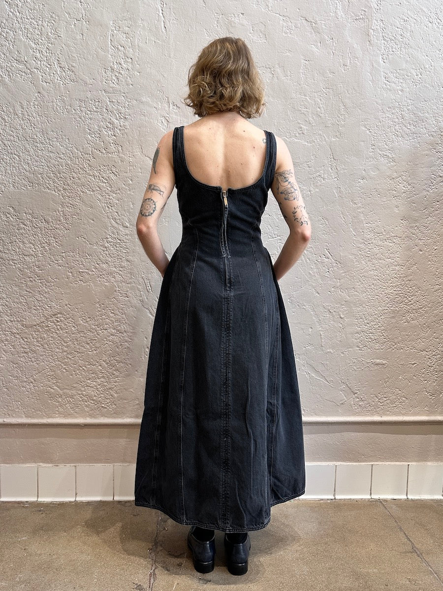 Person wearing a black denim dress standing against a plain wall.