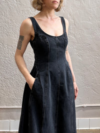 Person wearing a black sleeveless denim dress against a plain wall.