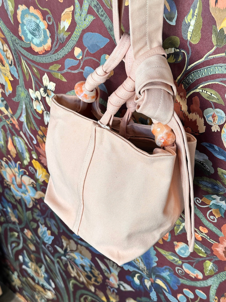 pink handbag with decorative strap accents against a patterned fabric background