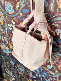 pink handbag with decorative strap accents against a patterned fabric background
