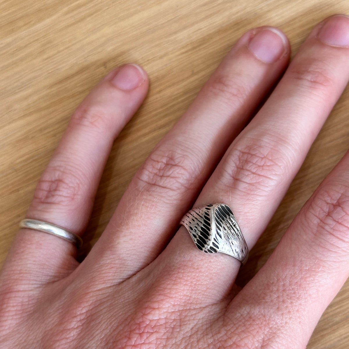 Hand wearing a silver ring on a wooden surface
