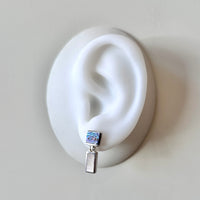 Silver earring with colorful abalone and pearl inlay on a white ear model against a light gray background