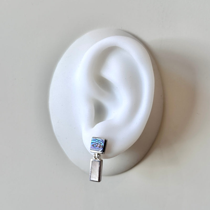 Silver earring with colorful abalone and pearl inlay on a white ear model against a light gray background