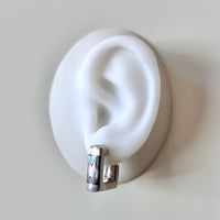 Silver earring on a white ear model against a light gray background