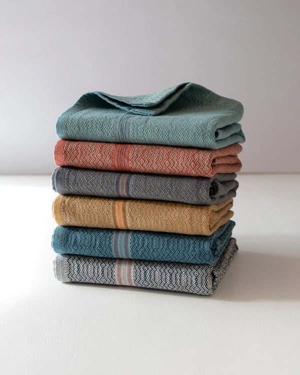 Stack of folded textured towels in various colors on a white surface with a light gray background