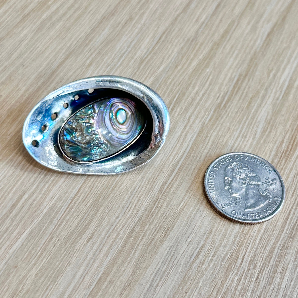 Silver brooch with a central gemstone next to a U.S. quarter on a wooden surface