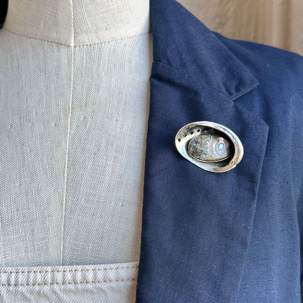 Close-up of a blue jacket with a silver brooch on a neutral background