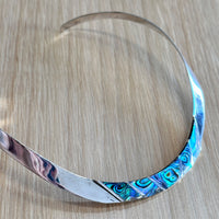 Silver choker with blue and green abalone inlay on a wooden surface