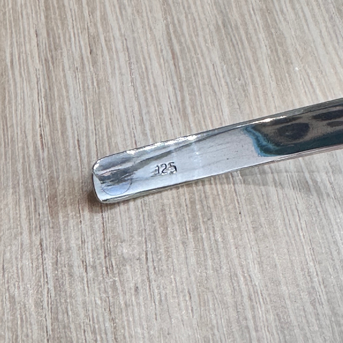 end of a silver necklace with '925' engraving on a wooden surface