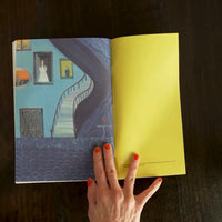 Open magazine with a staircase illustration on a dark surface, held open by a hand.