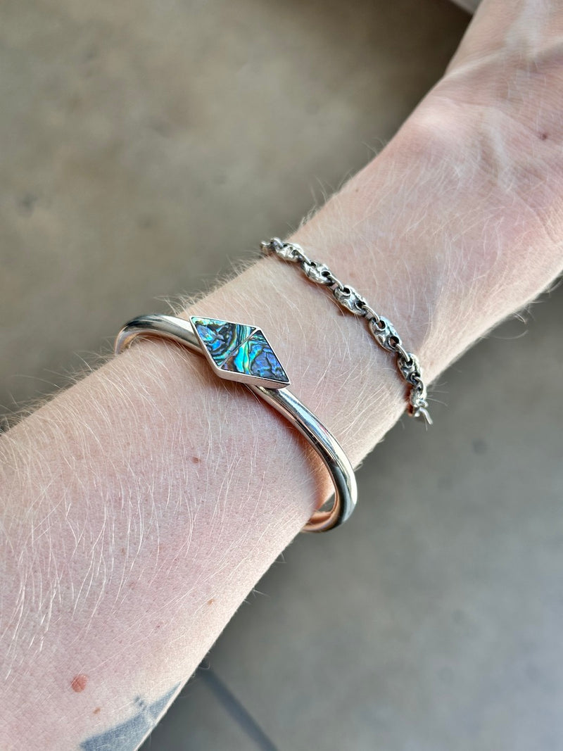 Silver bracelet with abalone inlay on a wrist against a neutral background