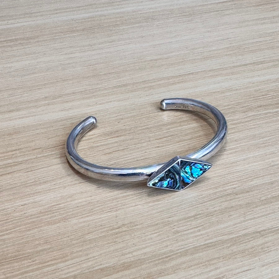 Silver bracelet with abalone inlay on a wooden surface