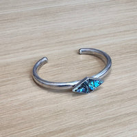 Silver bracelet with abalone inlay on a wooden surface
