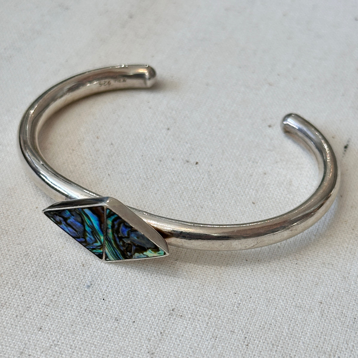 Silver bracelet with a geometric abalone stone on a light fabric background