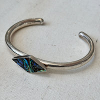 Silver bracelet with a geometric abalone stone on a light fabric background