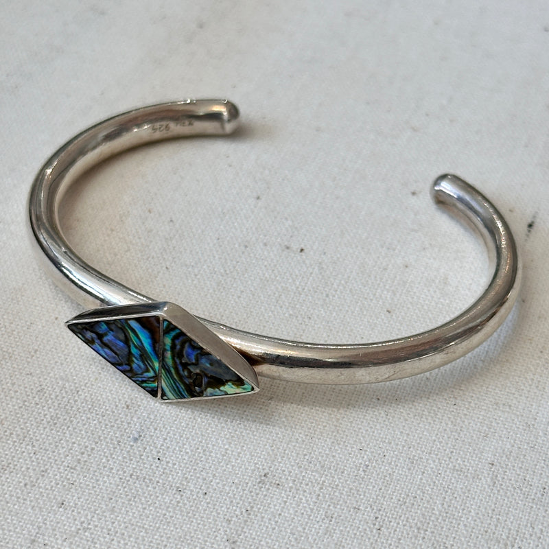 Silver bracelet with a geometric abalone stone on a light fabric background