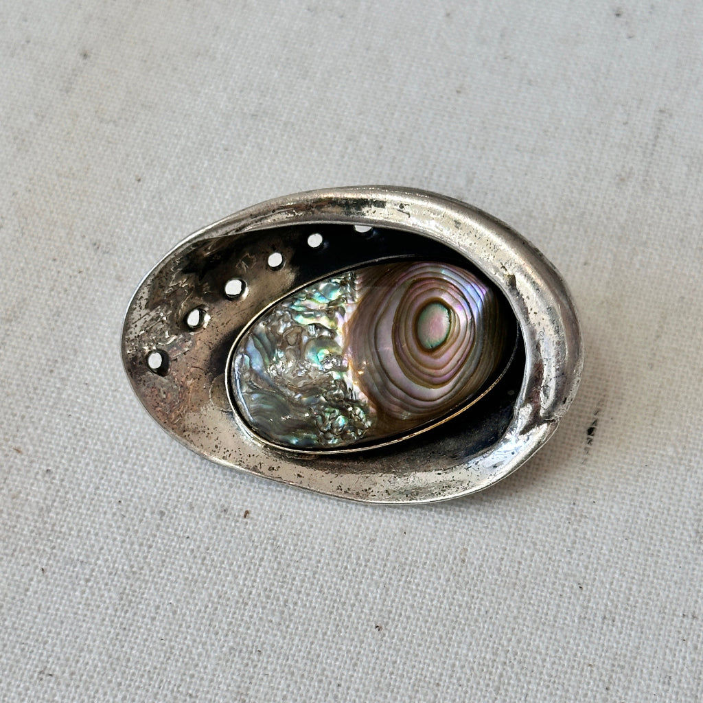 Decorative silver brooch with abalone shell inside on a textured surface