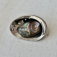 Decorative silver brooch with abalone shell inside on a textured surface