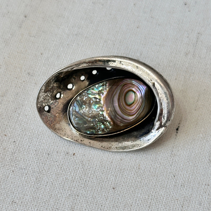 Decorative silver brooch with abalone shell inside on a textured surface