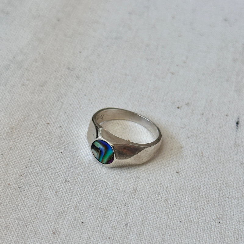 Silver ring with abalone inlay on a textured fabric background