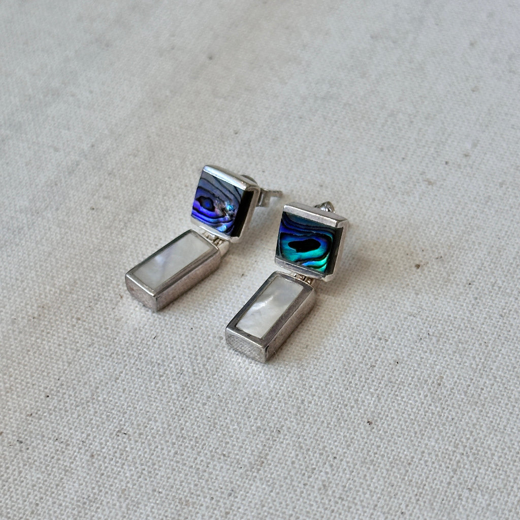 Pair of silver earrings with abalone and mother of pearl inlays on a light fabric background