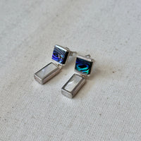 Pair of silver earrings with abalone and mother of pearl inlays on a light fabric background