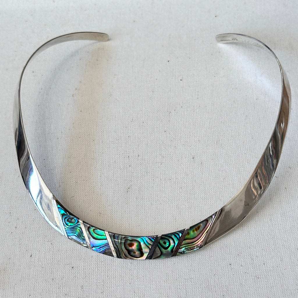 Silver choker with abalone shell inlay on a light fabric background