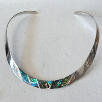 Silver choker with abalone shell inlay on a light fabric background