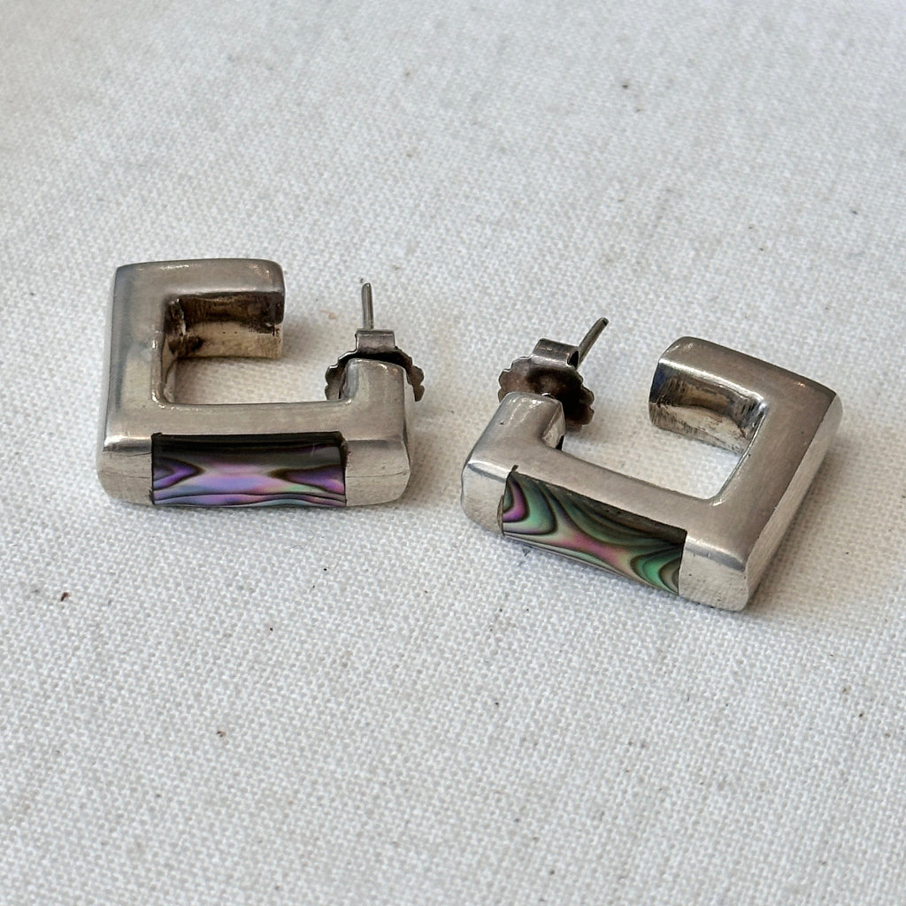 Pair of silver square hoop earrings with colorful abalone inlays on a light fabric background