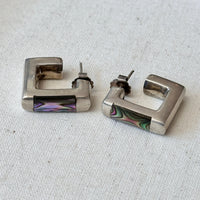 Pair of silver square hoop earrings with colorful abalone inlays on a light fabric background