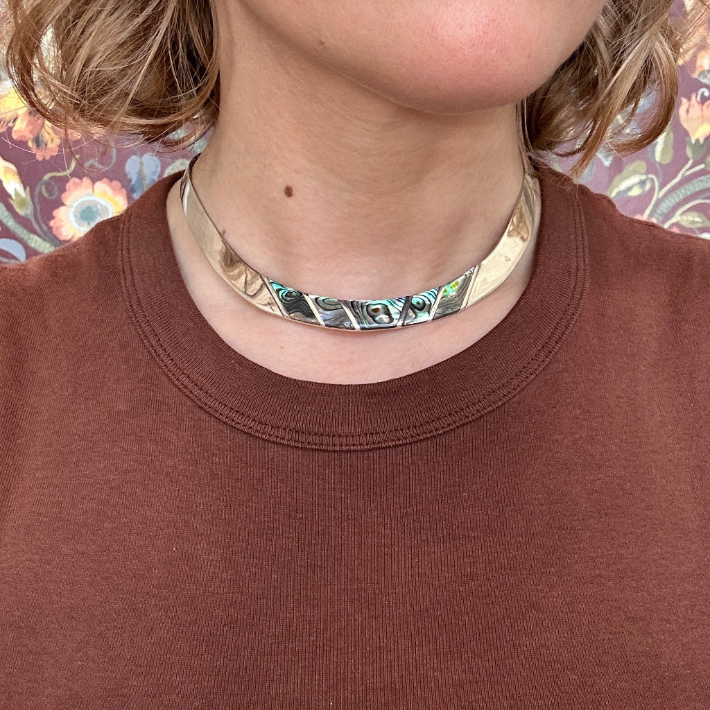 Person wearing a silver and abalone choker necklace with a brown shirt against a floral background