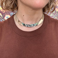 Person wearing a silver and abalone choker necklace with a brown shirt against a floral background