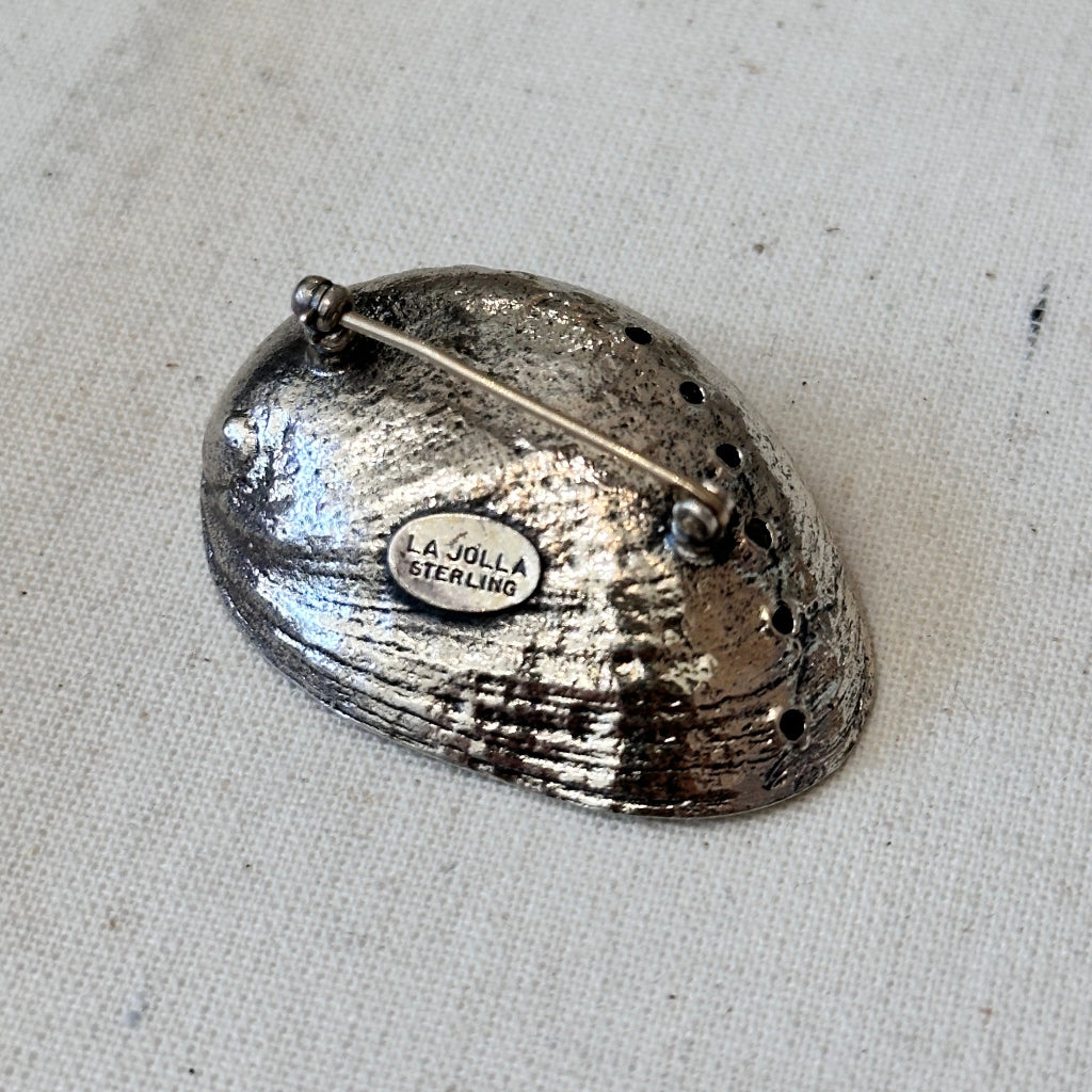 Silver shell brooch with 'La Jolla Sterling' stamp on a textured beige background