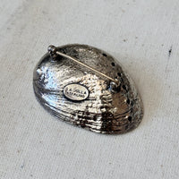 Silver shell brooch with 'La Jolla Sterling' stamp on a textured beige background
