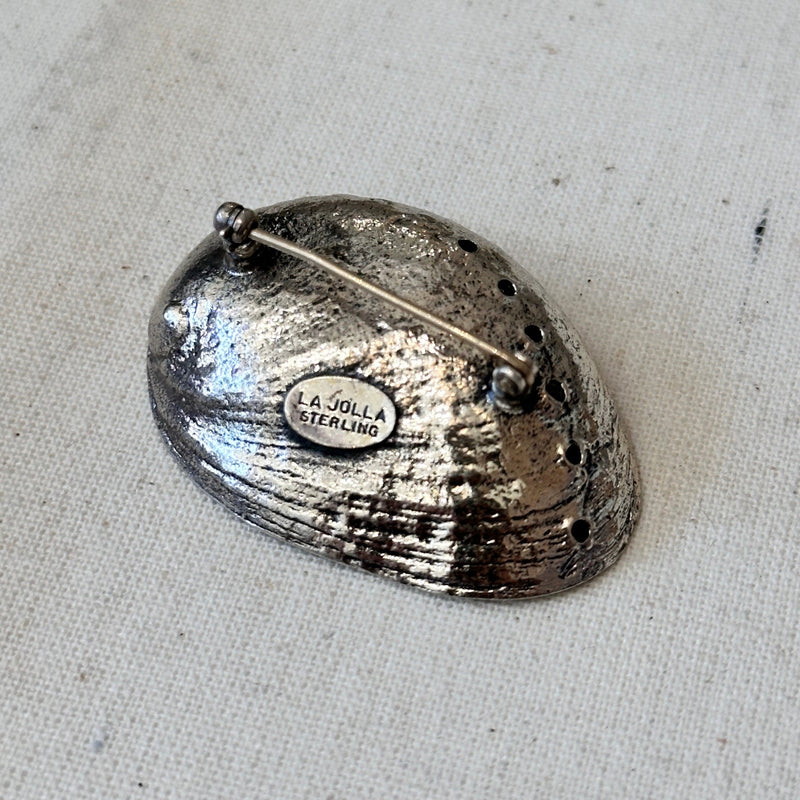 Silver shell brooch with 'La Jolla Sterling' stamp on a textured beige background