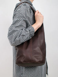 Person with a polka dot shirt wearing a dark brown leather bag over one shoulder against a plain background