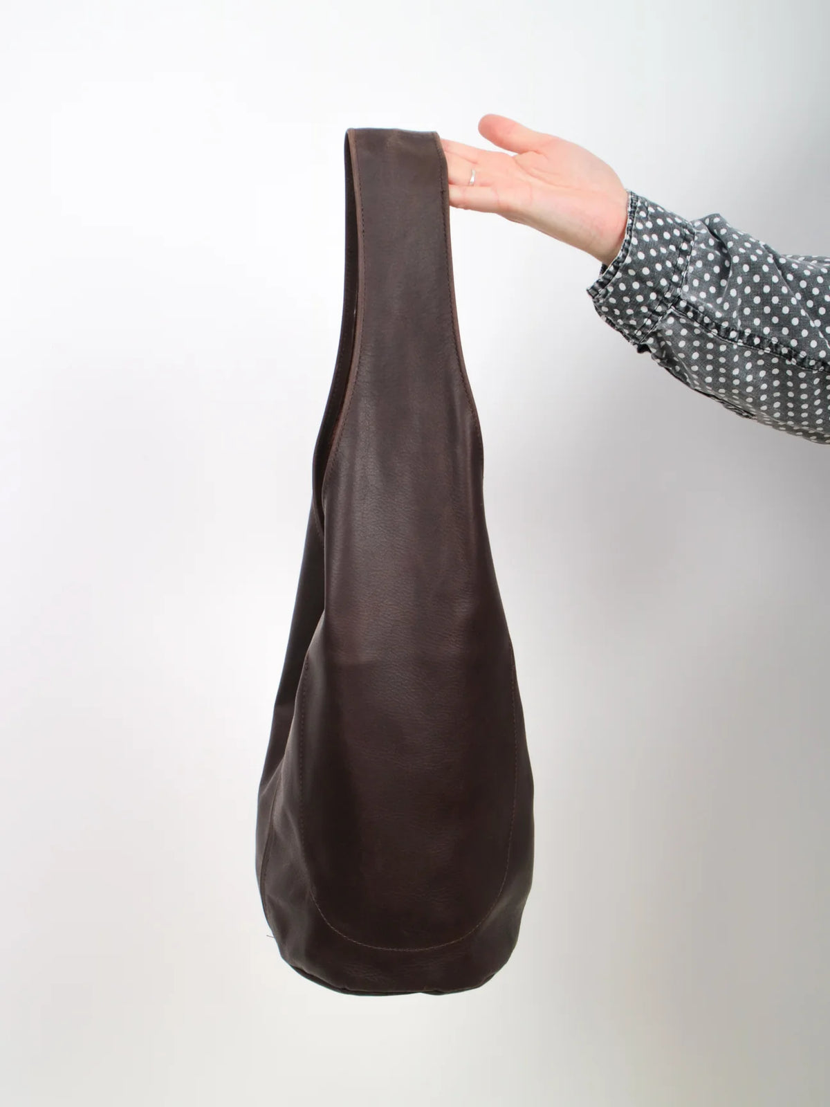 Dark brown leather bag held by a hand against a white background