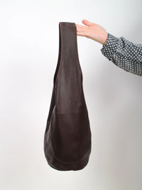 Dark brown leather bag held by a hand against a white background