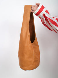 Brown leather bag held by a person wearing a red and white striped shirt on a light gray background