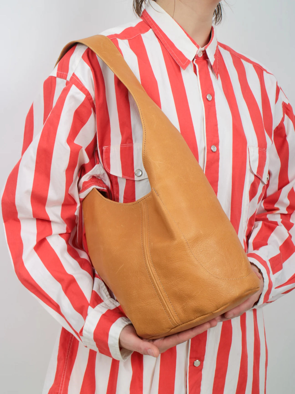 Person wearing a red and white striped shirt holding a tan leather bag over their shoulder