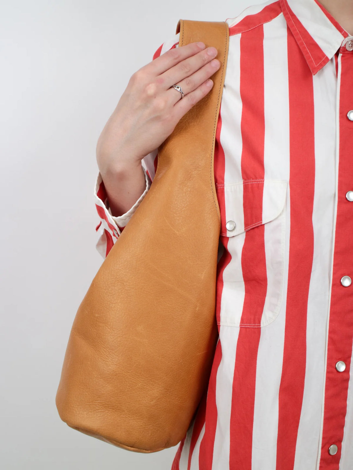 Person holding a brown leather bag on their shoulder against a white background