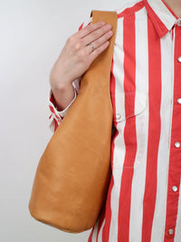 Person holding a brown leather bag on their shoulder against a white background