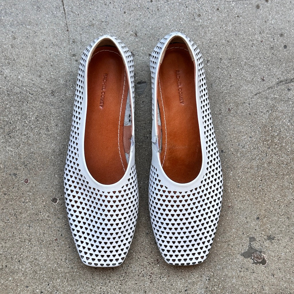 Top view of white perforated leather flats on a concrete surface