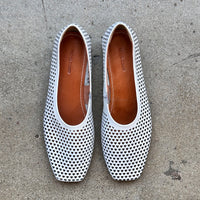 Top view of white perforated leather flats on a concrete surface