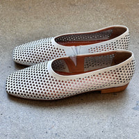 Side view of white perforated leather flats on a concrete surface