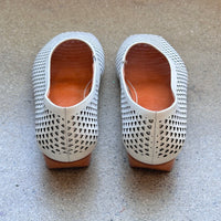 Back view of white perforated leather flats on a concrete surface