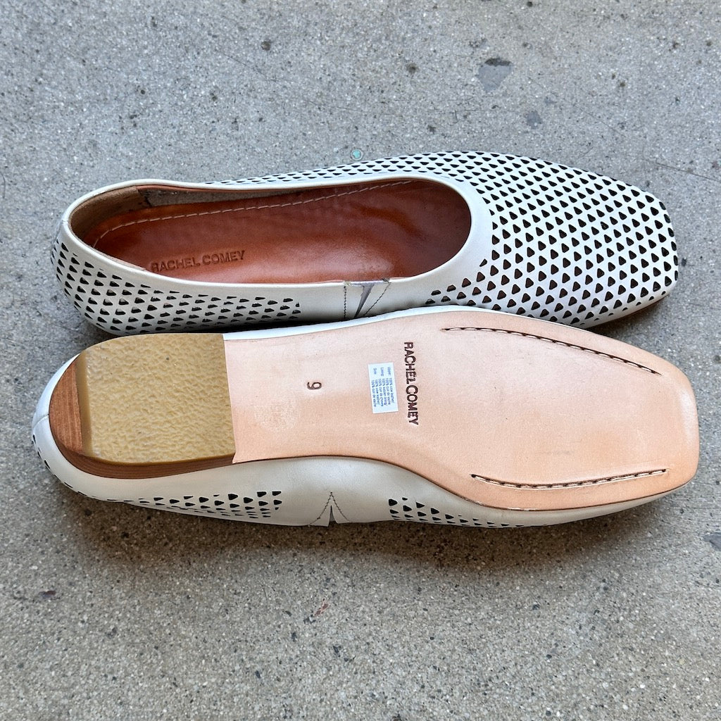Top and bottom view of white perforated leather flats by Rachel Comey on a concrete surface